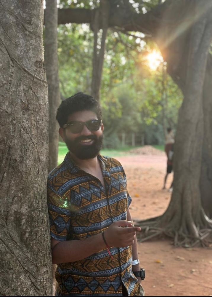 Pratham leaning against a banyan tree at sunset, smiling