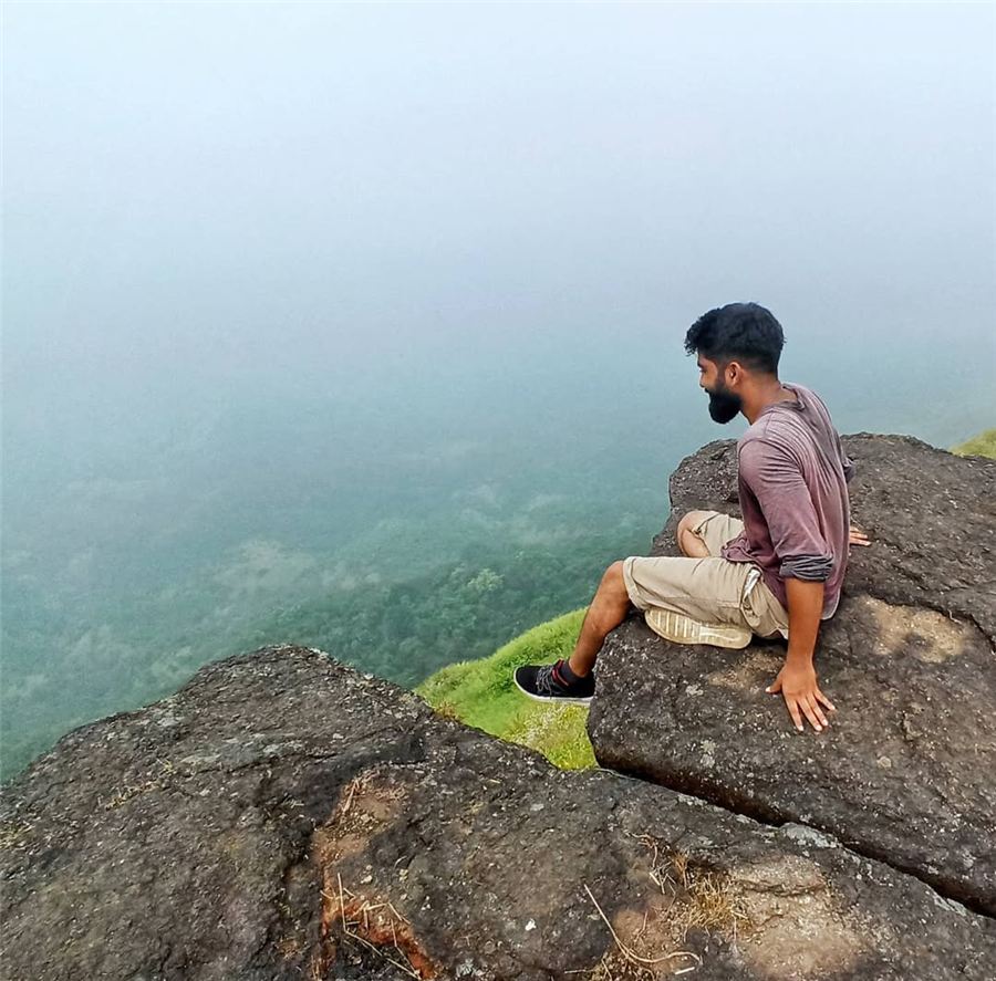 Pratham sitting on a rocky cliff edge above monsoon fog