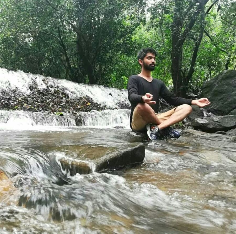 Pratham meditating cross-legged on a rock in the middle of a stream